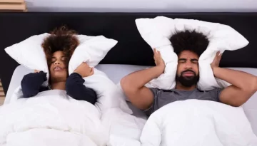 Elevated View Of Young Couple Lying In Bed Covering Their Ears With Pillow